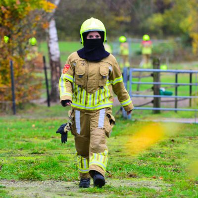 Brandweervrouw in uitrukkleding van Brandweer Meijel, ze loopt in een weiland en kijkt recht in de camera.