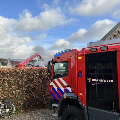 Tankautospuit van Brandweer Echt schuin in beeld. Op de achtergrond woedt een brand, die wordt bestreden door een hoogwerker